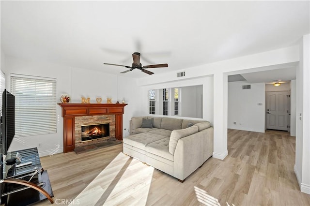 living room with light wood-type flooring, ceiling fan, and a stone fireplace