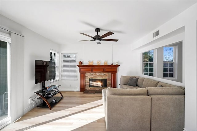 living room featuring ceiling fan, light wood-type flooring, and a fireplace