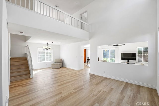 unfurnished living room featuring light wood-type flooring, a healthy amount of sunlight, ceiling fan with notable chandelier, and a towering ceiling