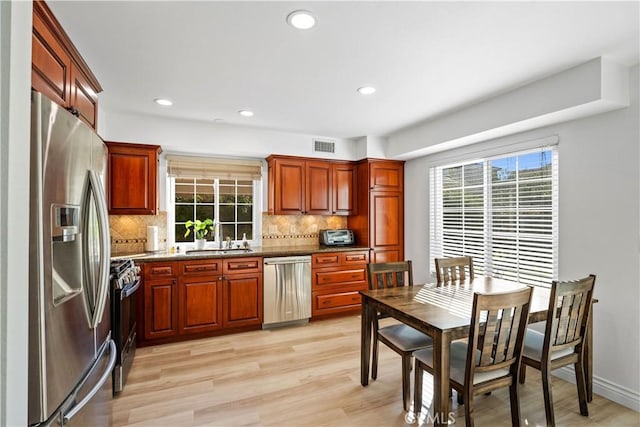 kitchen with appliances with stainless steel finishes, dark stone counters, tasteful backsplash, sink, and light hardwood / wood-style flooring