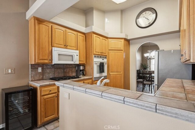 kitchen with wine cooler, tile counters, a towering ceiling, stainless steel appliances, and backsplash