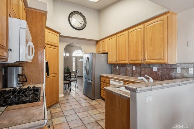 kitchen with tasteful backsplash, tile countertops, black gas cooktop, and stainless steel fridge with ice dispenser