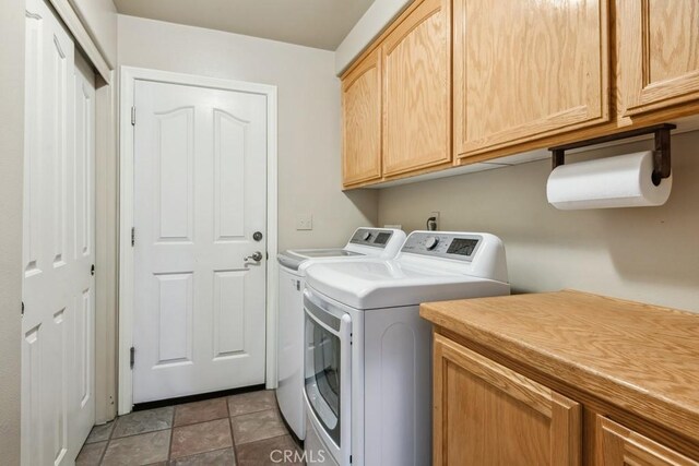 clothes washing area featuring washer and dryer, light tile patterned floors, and cabinets