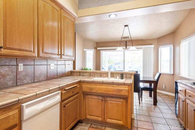 kitchen featuring tasteful backsplash, dishwasher, sink, hanging light fixtures, and tile counters