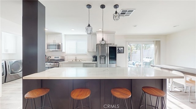 kitchen with a breakfast bar, decorative light fixtures, appliances with stainless steel finishes, light stone countertops, and white cabinets