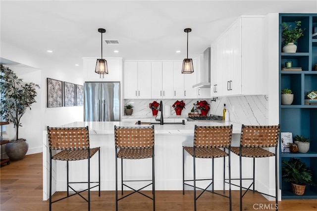 kitchen with kitchen peninsula, decorative light fixtures, stainless steel fridge, and wall chimney range hood