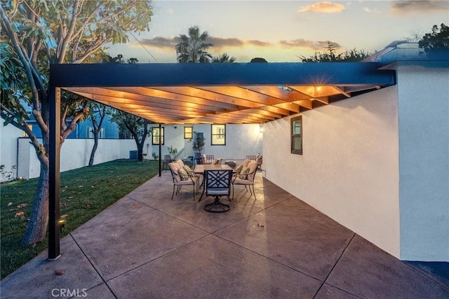 patio terrace at dusk featuring a pergola and a yard