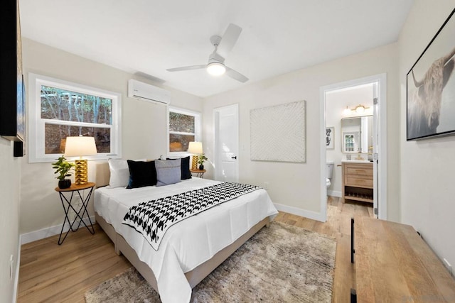 bedroom with ensuite bath, light hardwood / wood-style flooring, a wall mounted AC, and ceiling fan