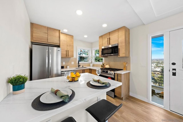 kitchen featuring backsplash, sink, light wood-type flooring, a breakfast bar area, and stainless steel appliances