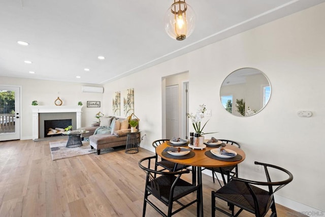 dining room with a wall mounted air conditioner, light hardwood / wood-style floors, and a fireplace