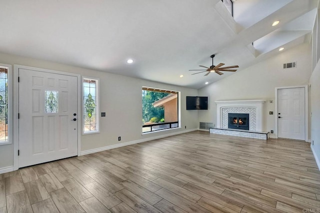 unfurnished living room featuring light wood-type flooring, ceiling fan, vaulted ceiling with skylight, and a tile fireplace