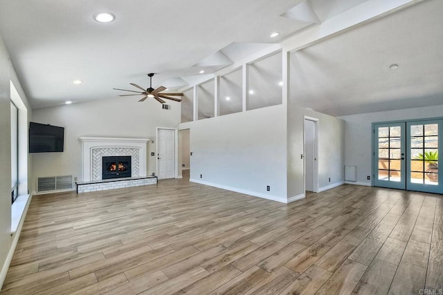 unfurnished living room with french doors, beamed ceiling, light hardwood / wood-style floors, ceiling fan, and a tile fireplace