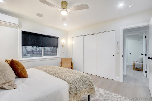 bedroom with ceiling fan, light hardwood / wood-style floors, a closet, and a wall mounted AC