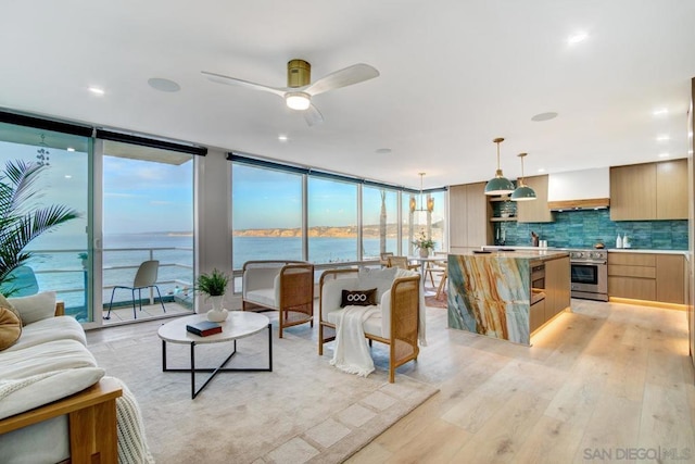 living room featuring ceiling fan, a water view, light wood-type flooring, and a wall of windows