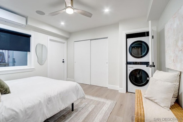 bedroom with an AC wall unit, stacked washer and dryer, ceiling fan, light hardwood / wood-style floors, and a closet