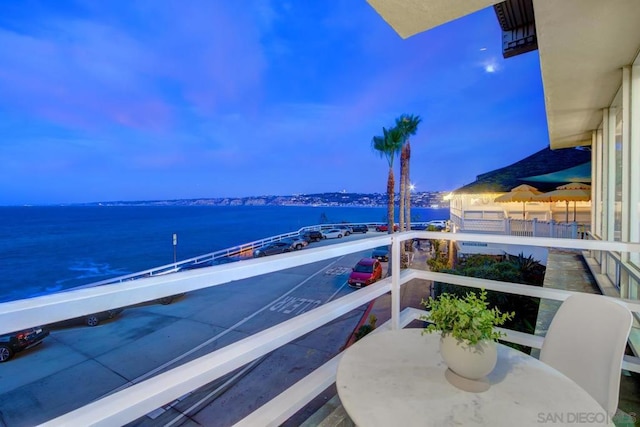 balcony at dusk featuring a water view