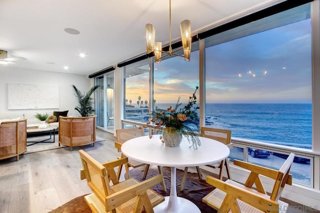 dining area featuring hardwood / wood-style floors, ceiling fan with notable chandelier, a view of the beach, floor to ceiling windows, and a water view