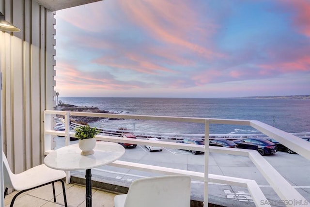 balcony at dusk featuring a water view