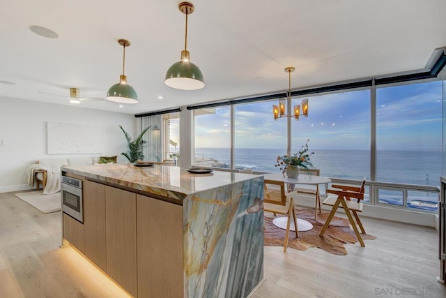 kitchen with pendant lighting, a center island, floor to ceiling windows, a water view, and light stone countertops