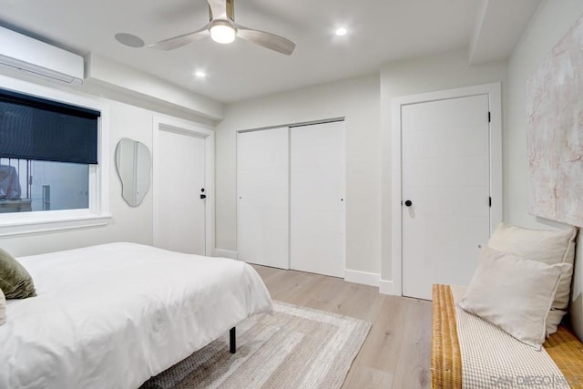 bedroom with light hardwood / wood-style flooring, a wall unit AC, a closet, and ceiling fan