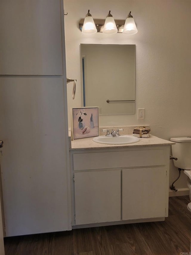 half bathroom with toilet, wood finished floors, and vanity