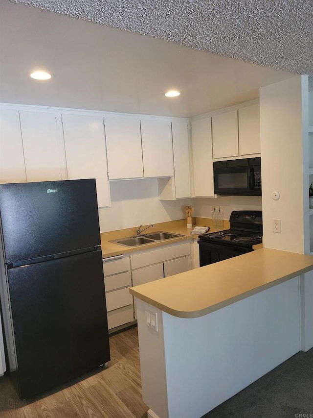 kitchen with a peninsula, a sink, white cabinetry, light countertops, and black appliances