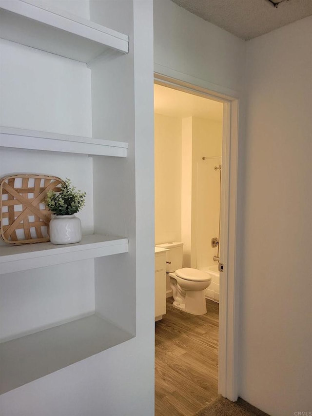 bathroom featuring toilet,  shower combination, wood finished floors, and vanity