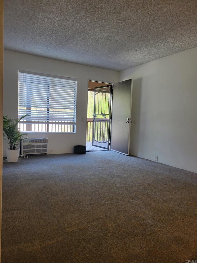 unfurnished room with a textured ceiling, carpet, and a wall unit AC