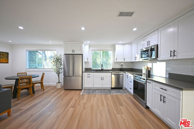 kitchen with light hardwood / wood-style floors, white cabinets, appliances with stainless steel finishes, and plenty of natural light