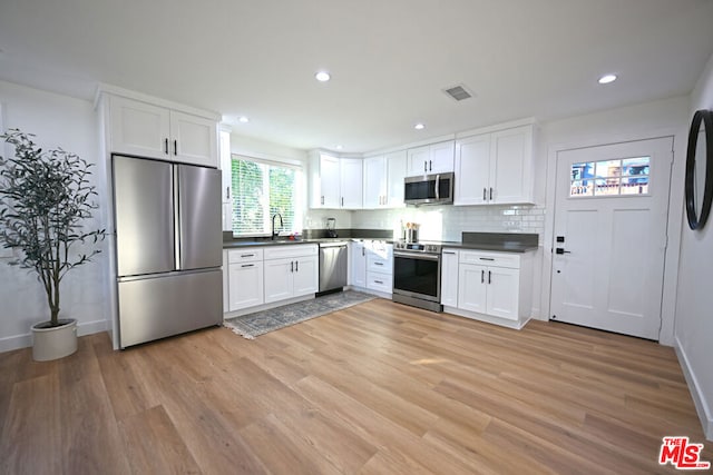 kitchen with light hardwood / wood-style floors, appliances with stainless steel finishes, backsplash, white cabinets, and sink