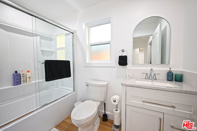 full bathroom with combined bath / shower with glass door, vanity, wood-type flooring, and toilet