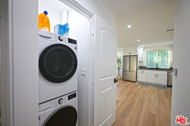 clothes washing area with light wood-type flooring, stacked washer and dryer, and sink