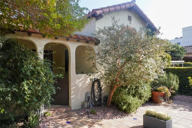 view of side of home featuring a tiled roof, a patio, and stucco siding