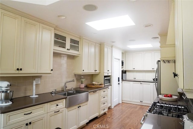 kitchen with cream cabinets, a sink, appliances with stainless steel finishes, light wood finished floors, and dark countertops