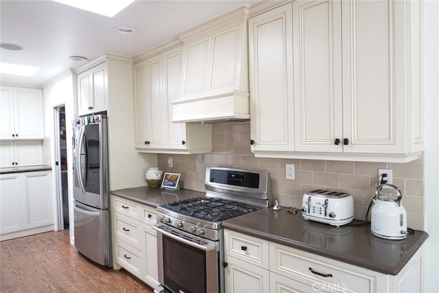 kitchen featuring appliances with stainless steel finishes, dark countertops, light wood-style floors, and decorative backsplash