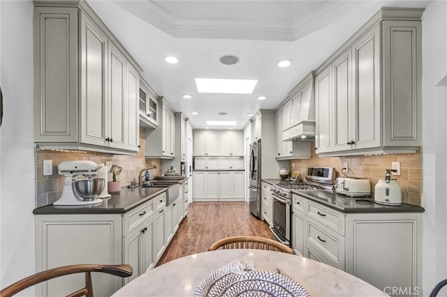 kitchen with a skylight, dark countertops, gray cabinetry, appliances with stainless steel finishes, and a sink