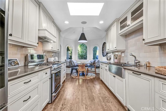 kitchen with light wood-style flooring, lofted ceiling with skylight, glass insert cabinets, stainless steel gas stove, and a sink