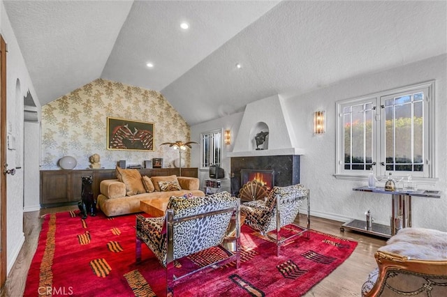 living area with a textured ceiling, a fireplace, wood finished floors, baseboards, and vaulted ceiling