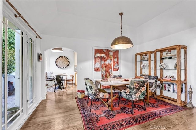 dining space with arched walkways and wood finished floors