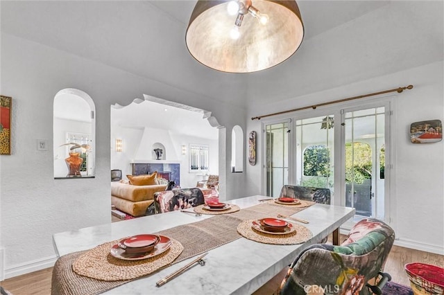 dining area with baseboards, arched walkways, wood finished floors, and a high end fireplace