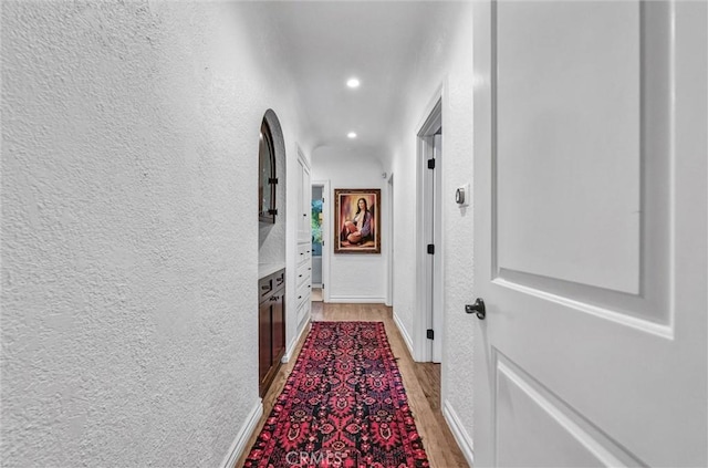 hallway with recessed lighting, baseboards, a textured wall, and light wood finished floors