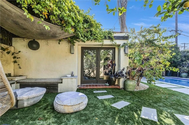 view of exterior entry with a yard, french doors, an outdoor pool, and stucco siding