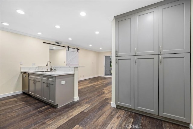 kitchen featuring a barn door, kitchen peninsula, gray cabinets, dark wood-type flooring, and sink