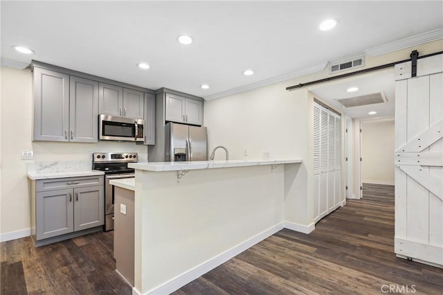 kitchen featuring a barn door, a kitchen bar, stainless steel appliances, gray cabinetry, and dark wood-type flooring