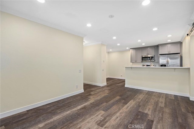 kitchen featuring dark hardwood / wood-style flooring, stainless steel appliances, gray cabinets, ornamental molding, and a barn door