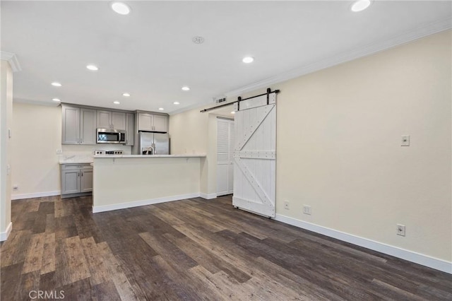 kitchen featuring a barn door, stainless steel appliances, gray cabinetry, dark wood-type flooring, and ornamental molding