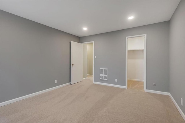 unfurnished bedroom with a walk in closet and light colored carpet