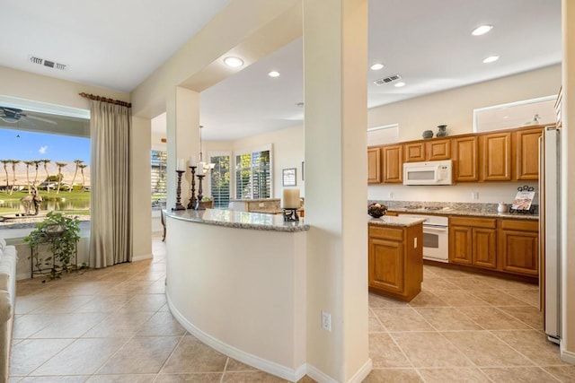 kitchen featuring hanging light fixtures, kitchen peninsula, light stone counters, and white appliances