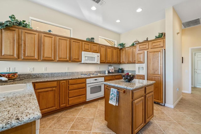 kitchen featuring light tile patterned floors, light stone countertops, white appliances, and a kitchen island