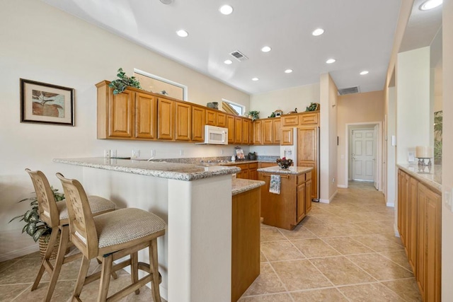 kitchen with light stone countertops, a kitchen island, paneled built in refrigerator, a kitchen breakfast bar, and kitchen peninsula